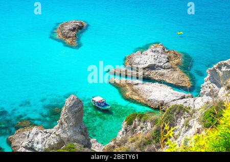 Yacht da pesca con ombre sul fondo della barca a vela e parco barca in gomma laguna blu azzurro acqua turchese superficie del mare tra rocce non lontano da capo Foto Stock