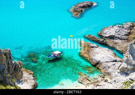 Yacht da pesca con ombre sul fondo della barca a vela e parco barca in gomma laguna blu azzurro acqua turchese superficie del mare tra rocce non lontano da capo Foto Stock