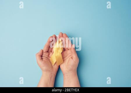 due mani femminili tengono nei loro palmi un nastro giallo sotto forma di un anello su uno sfondo blu, simbolo della lotta contro il tumore del gatto, problema Foto Stock