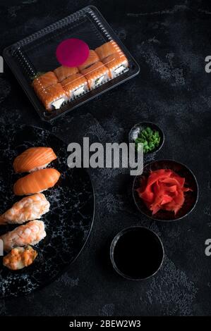 Delizioso sushi servito su ardesia di pietra scura. Sfondo nero. Set di rotoli di sushi in scatola di plastica, servizio di consegna Foto Stock