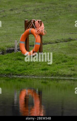 Una Lifebuoy su una corda a lato di un grande stagno. Foto Stock