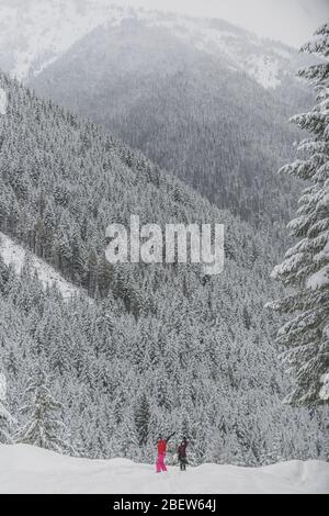 Due giovani donne che si muovono con la macchina fotografica da lontano nel Manning Park in inverno Foto Stock