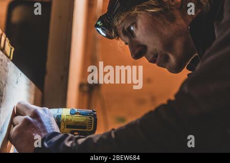 Primo piano di Man Drilling in legno in condizioni di scarsa illuminazione con lampada frontale Foto Stock