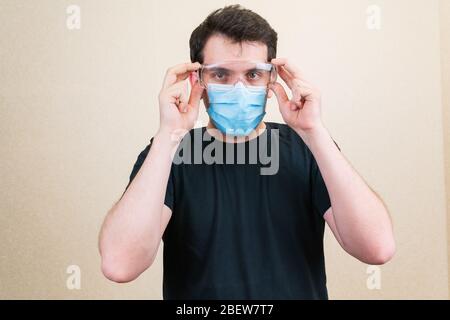 Giovane uomo in maschera medica protettiva e occhiali. Autoisolamento e quarantena. Rimani a casa Foto Stock