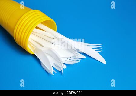 Stoviglie monouso in plastica su sfondo blu. Forcelle bianche e coltelli all'interno di tazze gialle Foto Stock