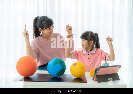 Scuola elementare asiatica con madre che dipinge la luna in classe di scienza imparare circa il sistema solare tramite video conferenza con l'insegnante e altro Foto Stock