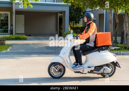 Corriere asiatico uomo su scooter che consegna il cibo nelle strade della città con una consegna di cibo caldo da prendere in viaggio e ristoranti a casa, espresso consegna di cibo a Foto Stock