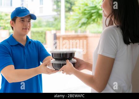 Asian consegna giovane uomo in blu uniforme sorriso e tenere scatole di cibo in casa e donna asiatica accettare una consegna di scatole di cibo da consegnare Foto Stock