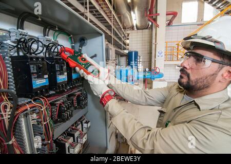 Tecnico elettrico messicano che esegue la manutenzione ad un pannello di controllo elettrico del motore nel settore geotermico. Apprendista di lavori qualificati. Foto Stock