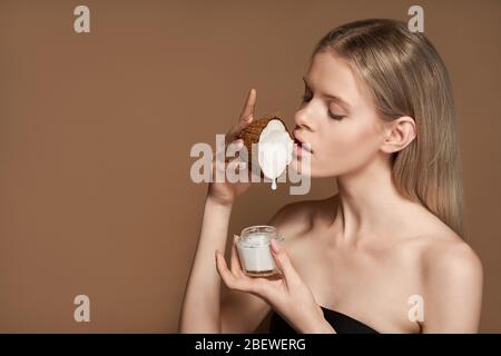 Bella donna tenere goccia olio di cocco caduta in vaso crema isolato sullo sfondo. Foto Stock