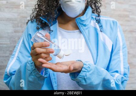 COVID-19 Donna che indossa la maschera facciale e che mette il gel di alcool sopra. Foto Stock