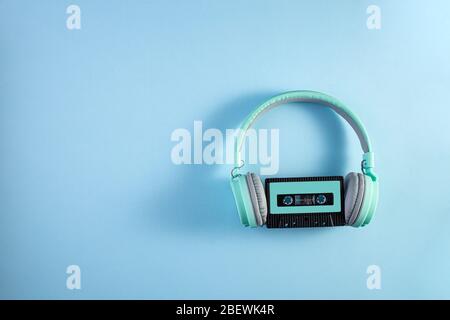 Cuffie turchesi con cassetta audio su sfondo blu. Concetto musicale con copyspace. Foto Stock