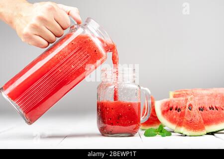 Succo di anguria in un bicchiere-fettine di anguria contro legno sfondo bianco Foto Stock