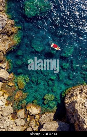 Antenna di barca nelle acque turchesi del mediterraneo. Una piccola barca vicino a rocce sparate dall'alto in Grecia, l'isola di Corfù. Foto Stock