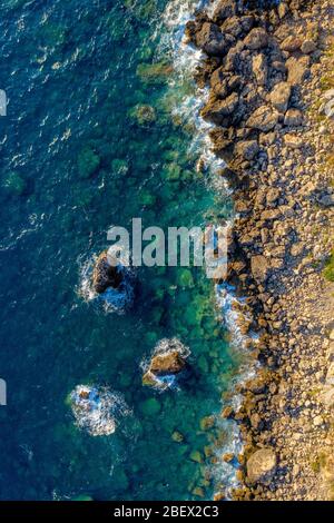 Antenna di onde oceaniche che colpiscono la costa rocciosa. Acqua di mare e rocce di colore torchese sparato dall'aria. Condimento da un drone Foto Stock