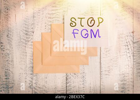 Testo di scrittura Stop FGM. Foto concettuale mettere una fine sul taglio genitale e circoncisione tre buste intorno a fogli di carta rigati vecchia vintage legno Foto Stock