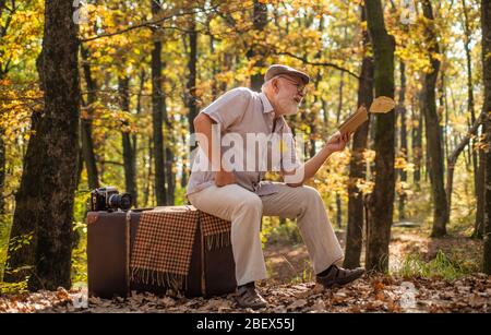 Avere il piacere di leggere di più. Pensionato leggere libro in autunno natura. Il vecchio leggeva seduto su una valigia retrò. Letteratura e biblioteca. Conoscenza e informazione. Gita naturalistica. Basta leggere bene. Foto Stock