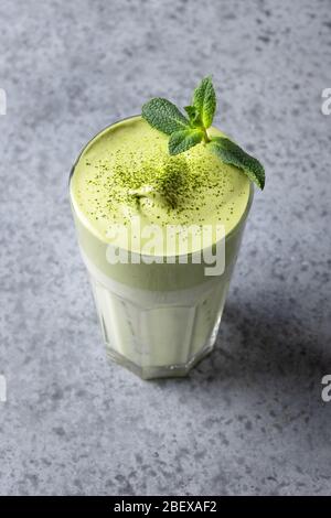 Dalgona Iced Matcha tè. Le uova bianche montate con il tè del matcha vengono aggiunte al latte con ghiaccio. Gustosa bevanda virale nel tempo autoisolamento. Formato verticale. Foto Stock