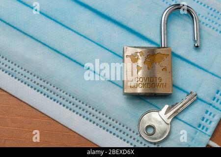 Fine di blocco del mondo del coronavirus: Un lucchetto aperto con una mappa del mondo e la parola lucchetto inciso e una chiave su una maschera chirurgica blu chiaro. Foto Stock