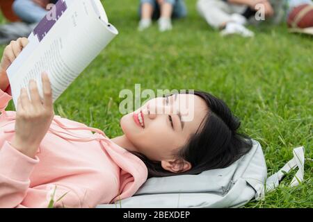 Gli studenti universitari si stendono sull'erba leggendo un libro Foto Stock