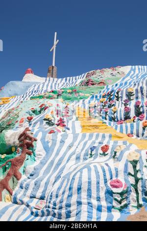Sentiero giallo che sale sulle colorate colline a strisce della montagna della salvezza con una croce sulla cima Foto Stock
