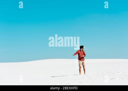 uomo sulla spiaggia sabbiosa con visore vr che si addorma contro il cielo azzurro Foto Stock