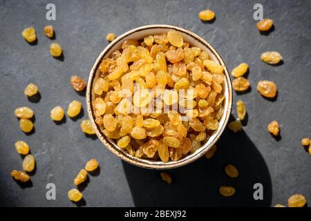 Uvetta dorata o sultana in ciotola su sfondo nero, vista dal piano del tavolo. Frutta secca, cibo sano per spuntini Foto Stock