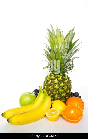 Una selezione di frutta tropicale su uno sfondo bianco, tra cui un ananas intero, mela verde, banana, arancia, limone a fette e un mazzo di Foto Stock