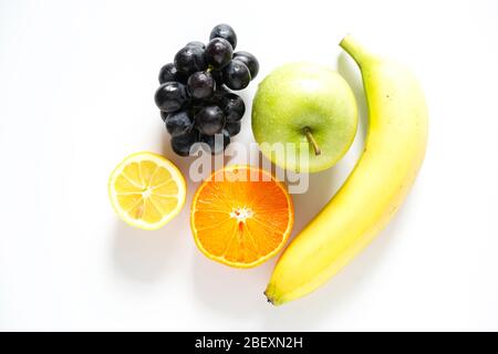 Una banana, mela smith grannosa, mezza arancia, mezza limone e un mazzo di uve nere su sfondo bianco Foto Stock