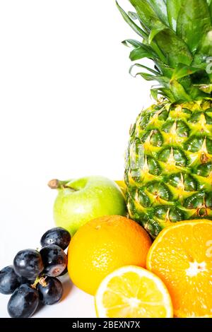 Una selezione di frutta tropicale su uno sfondo bianco, tra cui un ananas intero, mela verde, banana, arancia, limone a fette e un mazzo di Foto Stock
