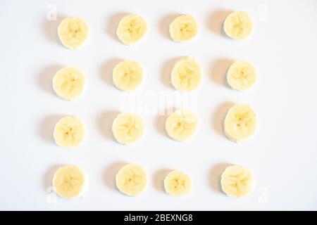 Una serie di pezzi di banana tagliati disposti in un disegno quadrato su uno sfondo bianco semplice Foto Stock