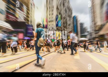 Folla offuscata di auto e tram con pedoni irriconoscibili che camminano intorno attraversando il quartiere Centrale in un'ora di punta giorno lavorativo, Hong Kong, bl Foto Stock