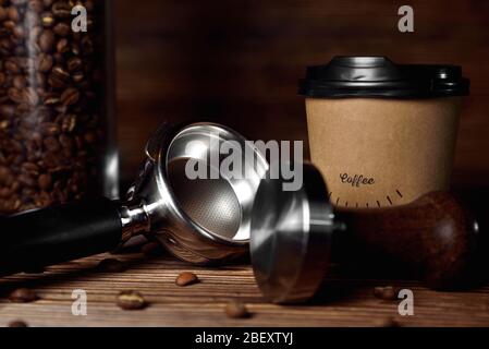 tempera la tazza di caffè in cartone con caffè in chicchi di caffè su uno spazio di copia da primo piano su sfondo di legno marrone Foto Stock