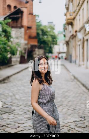 Sorridente, bella ragazza che cammina in città. Ragazza brunetta in estate vestire in tour della città. Giovane donna in un tour vista le belle strade del vecchio c. Foto Stock