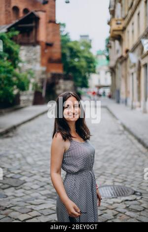 Sorridente, bella ragazza che cammina in città. Ragazza brunetta in estate vestire in tour della città. Giovane donna in un tour vista le belle strade del vecchio c. Foto Stock