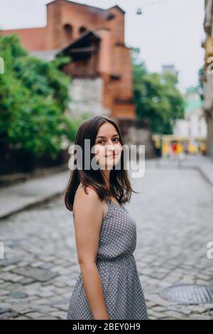 Sorridente, bella ragazza che cammina in città. Ragazza brunetta in estate vestire in tour della città. Giovane donna in un tour vista le belle strade del vecchio c. Foto Stock