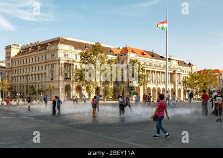 I turisti si rinfrescarono nella nebbia a Piazza Kossuth a Budapest, in Ungheria, con il Ministero dell'Agricoltura sullo sfondo Foto Stock