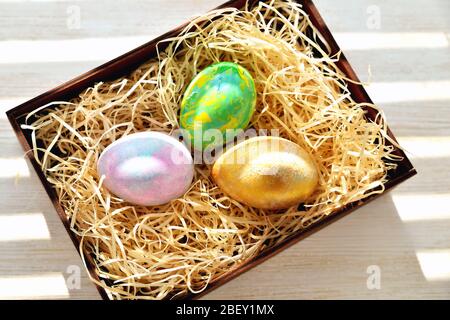 Tre uova di pollo colorate in una scatola con trucioli alla luce del sole Foto Stock