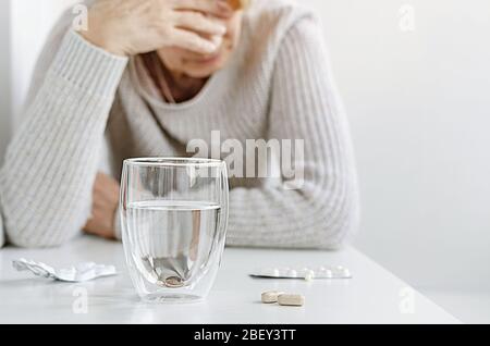 Donna anziana che soffre e che prende le pillole dall'emicrania. Concetto di trattamento della cefalea. Foto Stock