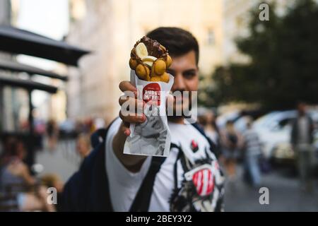 Giovane uomo che tiene una cialda a bolle con gelato e cioccolato. Cialda con frutta, cioccolato e gelato Foto Stock
