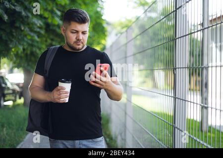 Un uomo con barba in una t-shirt nera con zaino usa un telefono Foto Stock