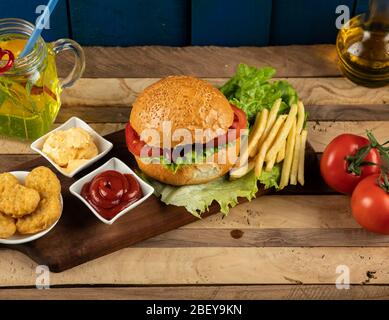 Hamburger, involtini di cipolle e patate fritte con salse e pomodori su un asse di legno Foto Stock