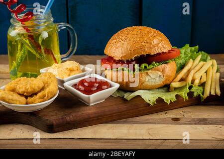 Hamburger, panini di cipolla e patate fritte con salse e pomodori serviti con un bicchiere di succo di frutta Foto Stock