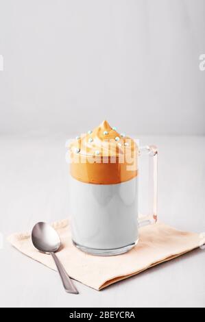 Dalgona Coffee decorato con spruzzi di Pasqua blu in una tazza di vetro su sfondo grigio chiaro. Il Dalgona Frothy Coffee è una bevanda coreana alla moda con frusta Foto Stock