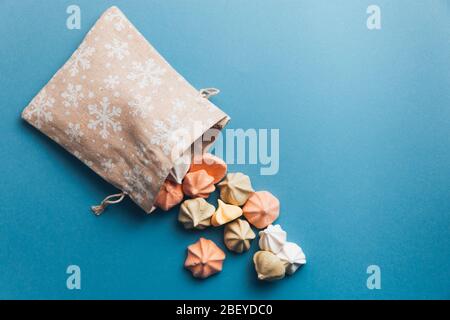 Meringhe colorate e una piccola borsa di stoffa decorata con fiocchi di neve bianchi su uno sfondo blu. Messa a fuoco selettiva. Foto Stock