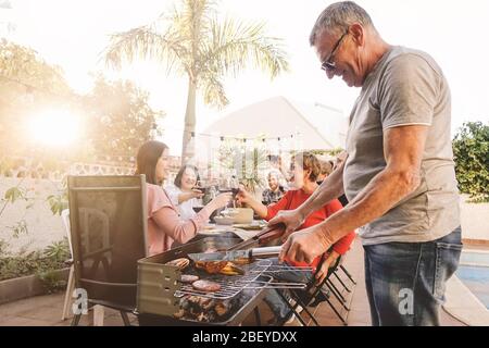 Buon piacere per la famiglia e tostare con vino rosso nel barbecue party - Chef uomo senior grigliare carne e divertirsi con i genitori Foto Stock