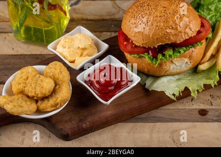 Hamburger, involtini di cipolle e patate fritte con salse su un asse di legno Foto Stock