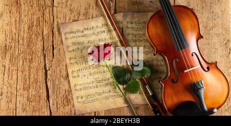 musica classica retrò violino string su vecchia musica nota foglio di carta con rosa fiore rosso su legno di quercia vecchio legno panorama copia spazio sfondo. c Foto Stock