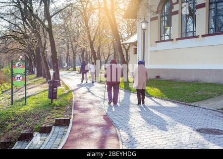 Le donne anziane e le giovani coppie camminano lungo il sentiero del parco. Una delle donne che usano i bastoni nordici. Nyiregyhaza, Ungheria Foto Stock