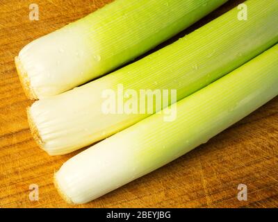 Tre porri freschi lavati su un tagliere di legno Foto Stock